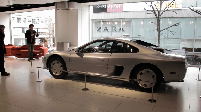 two people standing next to a sports car on display