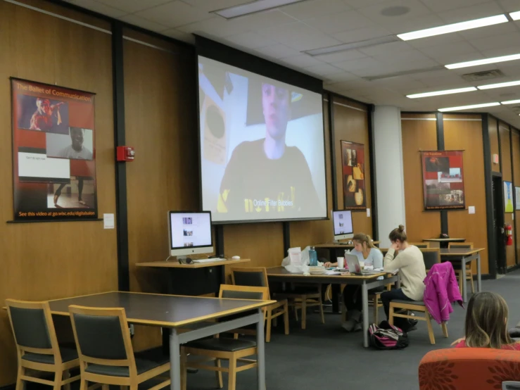 there are people that are standing and sitting in a room watching a screen