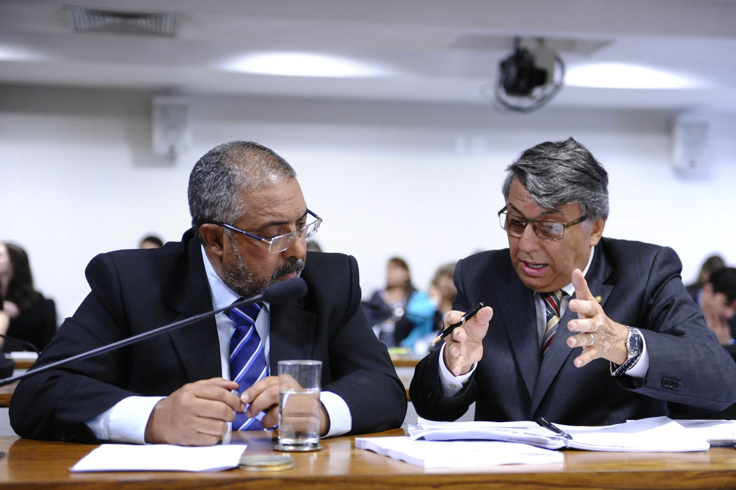 two men sitting at a table doing soing with their hands