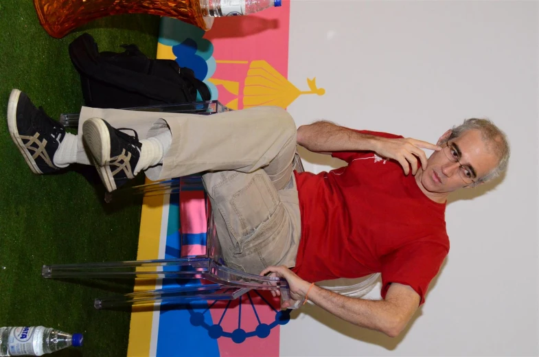 an old man in a red shirt and white pants sitting on a chair