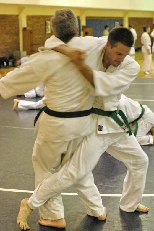 a man in white and a man with green belt are on a gym floor