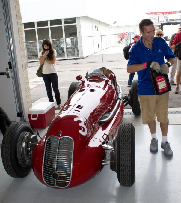 a man stands next to a racing car with two people in the background