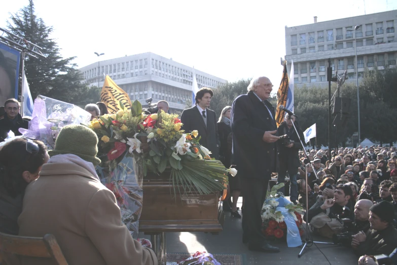 a group of men stand on a stage with flowers and flags