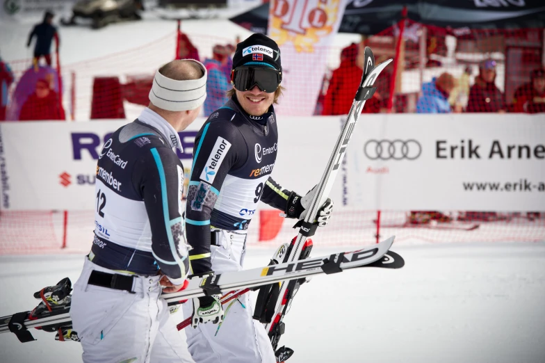 two men walking in front of a crowd holding skis