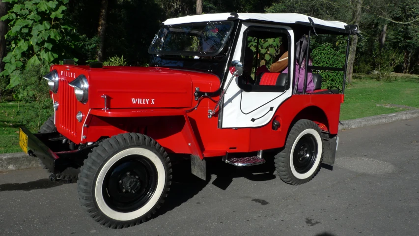 an old red truck is on a road near trees