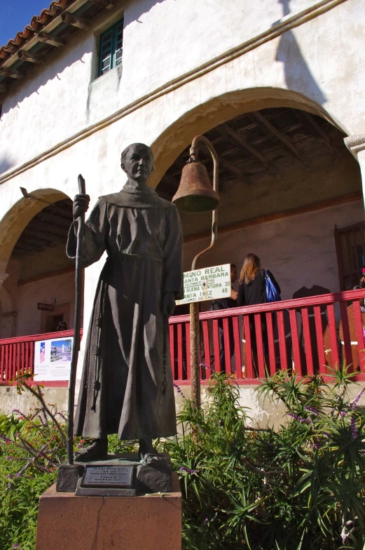 statue with bell outside building with people in background