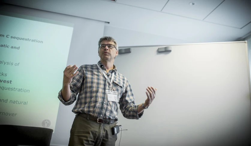 man speaking attentively in front of a large presentation screen