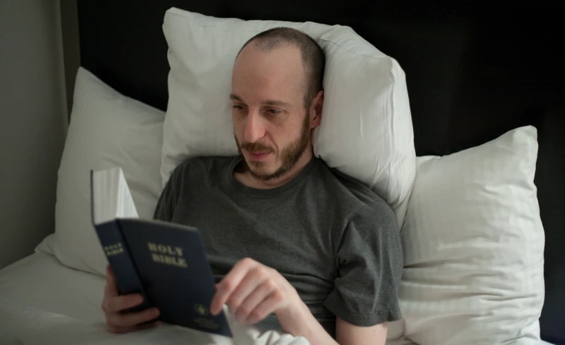 a man laying in bed looking at his book
