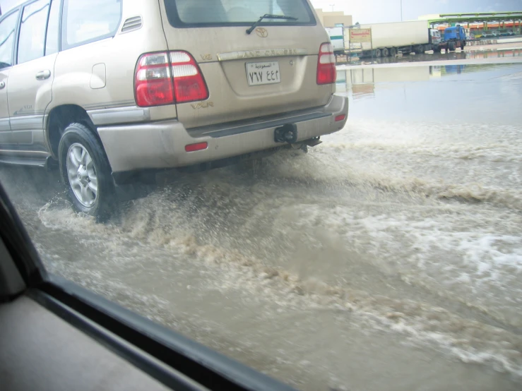 a parked car driving through some water on the side of a street