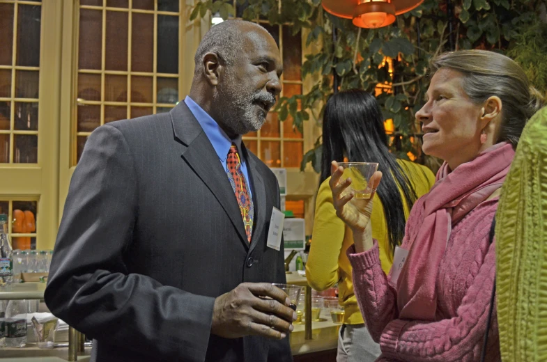 an old man drinking while two women talk around