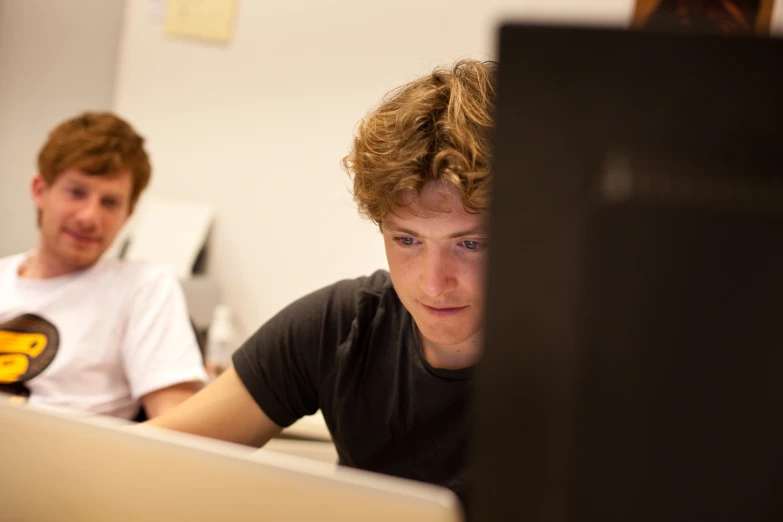 two young men are looking at the computer screen