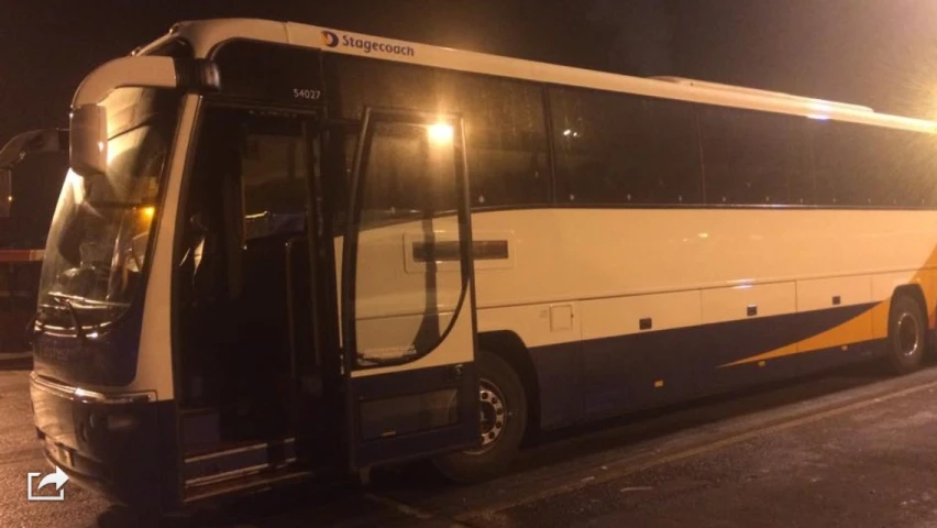 a white bus parked on the side of a road at night