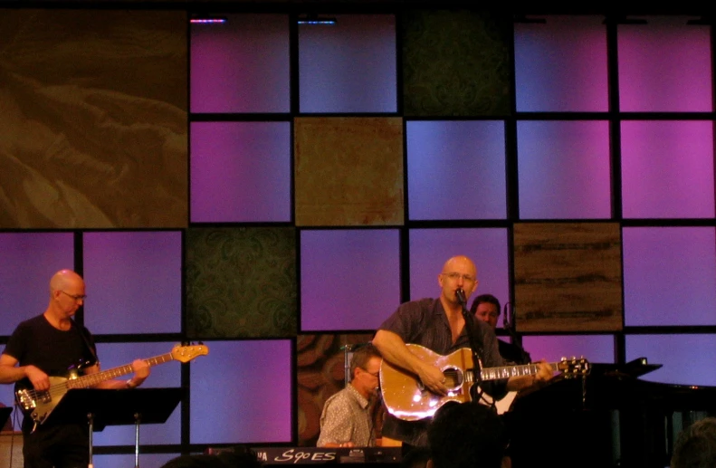 two men with guitar and a woman singing on stage