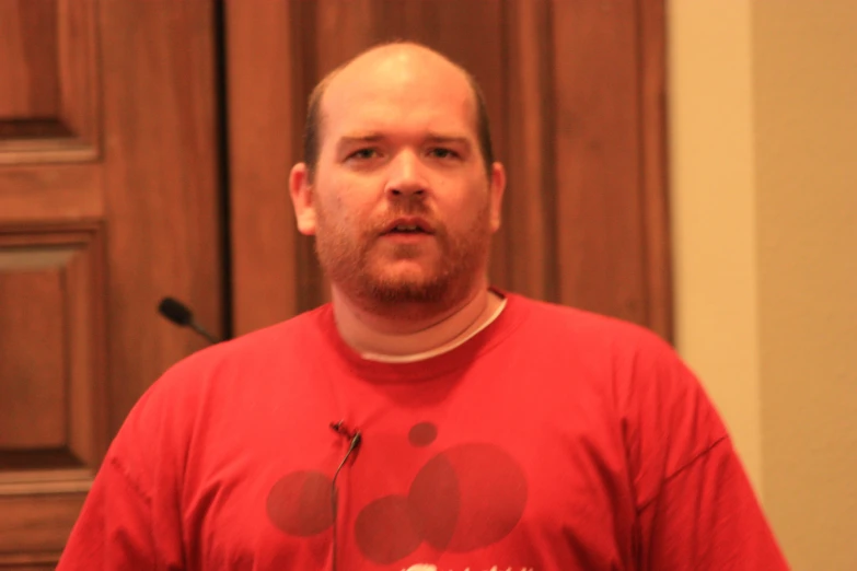 a man with a red shirt in front of wooden door