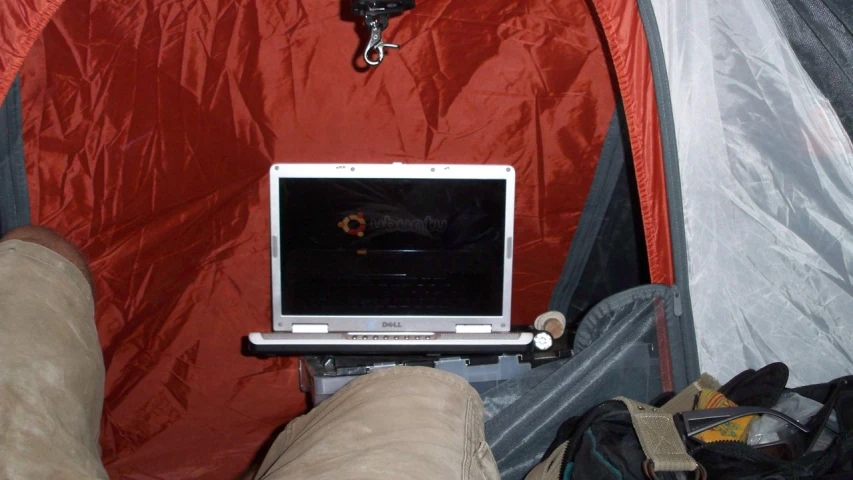 man's feet holding up a laptop in the tent