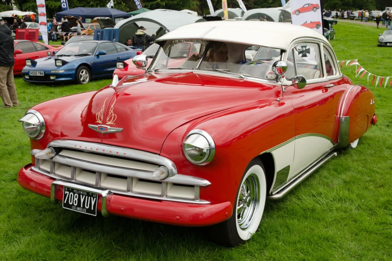 a vintage red and white car is parked on some grass