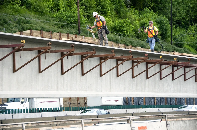 two construction workers walk on top of a large cement wall