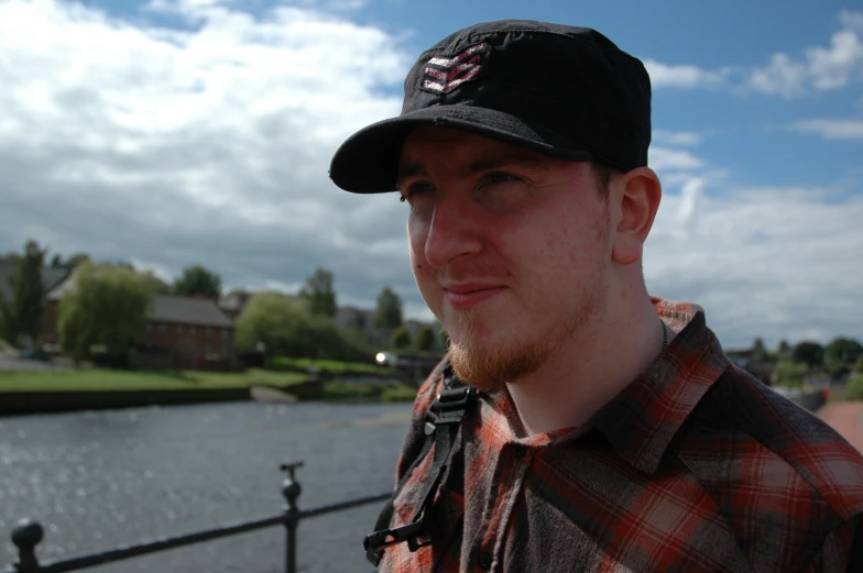 a man in a baseball cap stands near the water