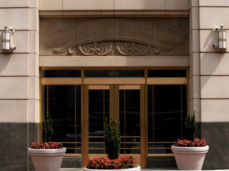 large white planters holding red flowers are in front of the entrance of a building