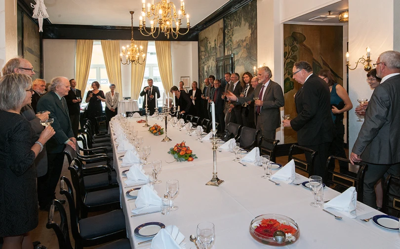 people in formal wear standing around a large dining table