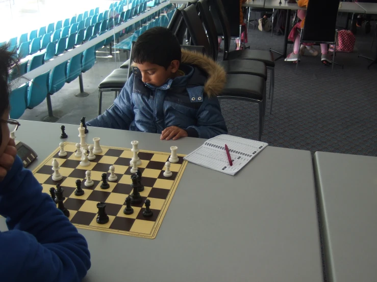 two young men play chess at a long table