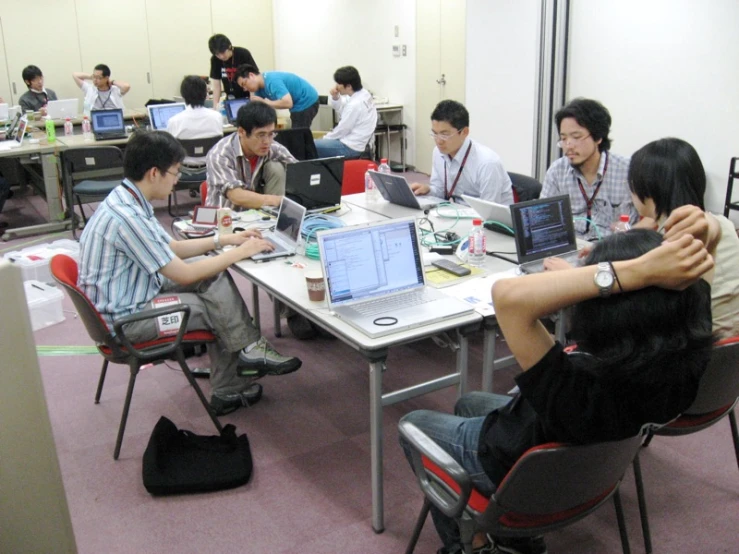 several people sitting in chairs around tables with laptop computers