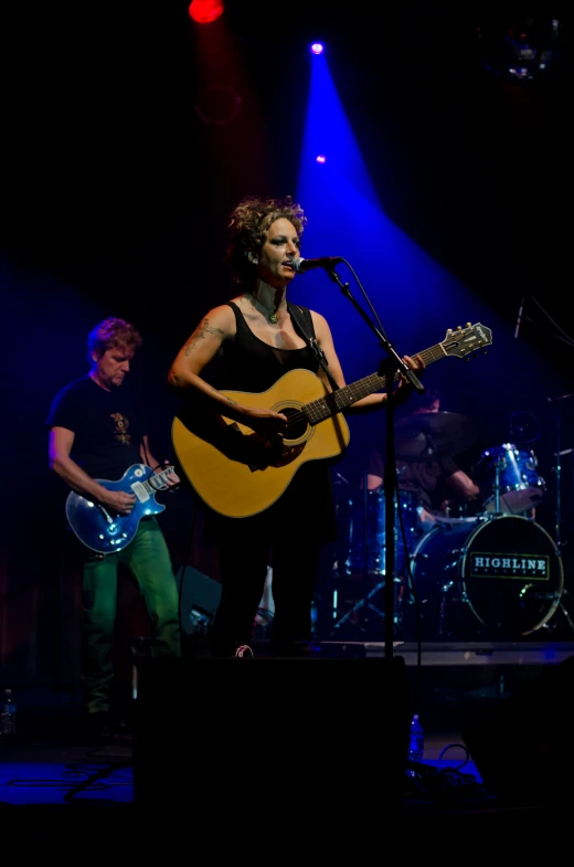 a woman singing in front of a microphone, guitar and other instruments