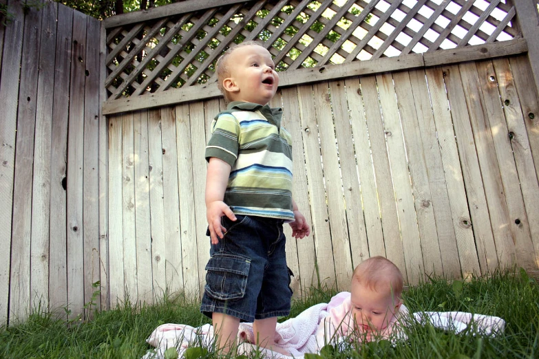 two young children stand near a fence in the grass