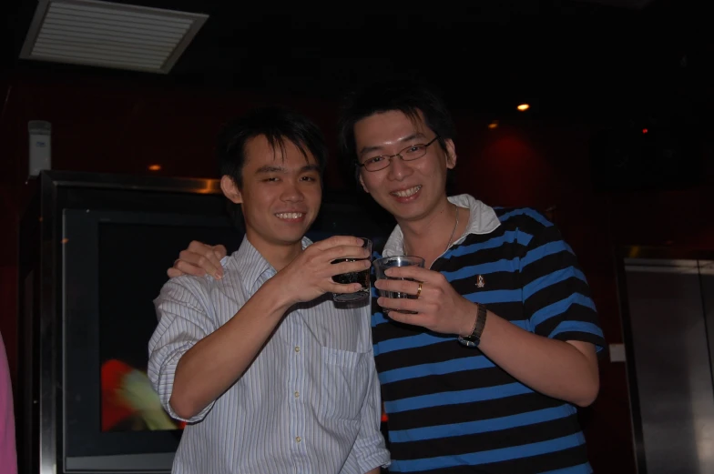 two young men are smiling while holding glasses