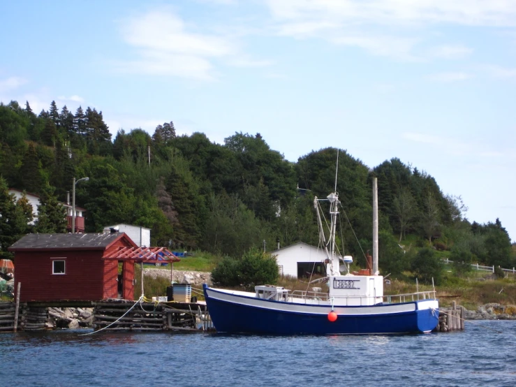 a blue and white boat sits in the water by a dock