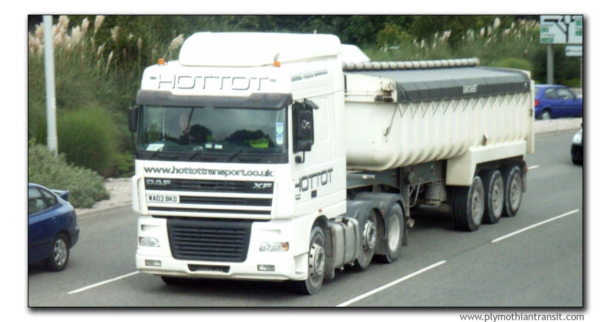 a white truck driving down a street next to a forest