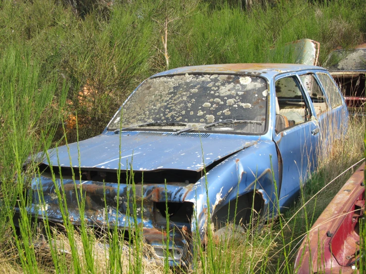 an old rusted car sitting in the grass