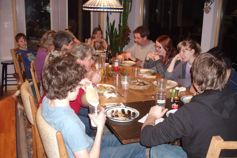 a group of people sitting around a wooden table eating food