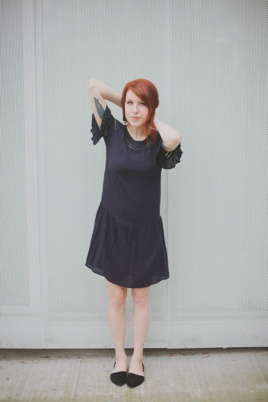 a woman posing in front of a white wall with her hair in a high bun