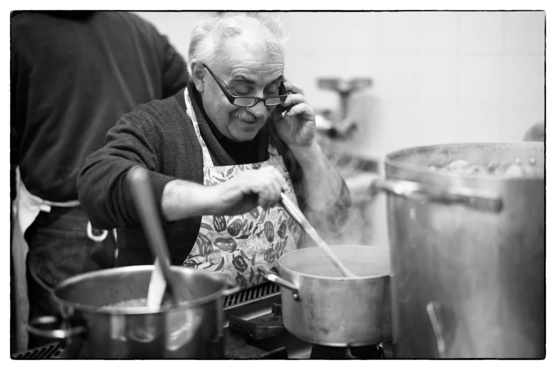 an old man wearing glasses talking on a cell phone cooking food