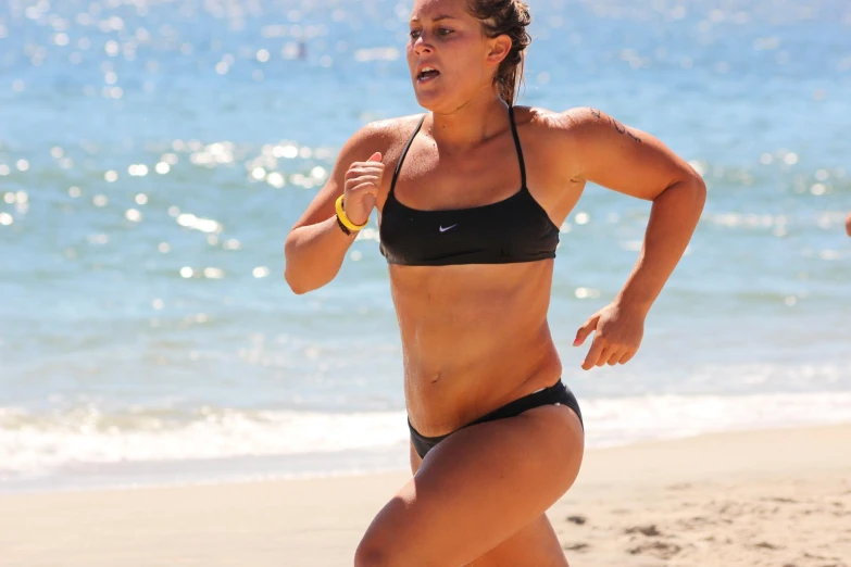 woman running along beach in a black bikini