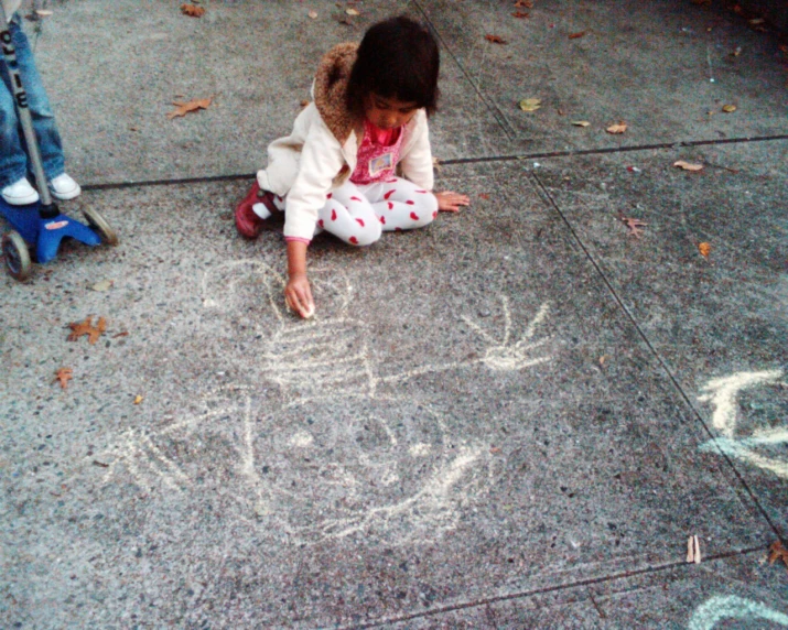 small child in white jacket playing with colored chalk