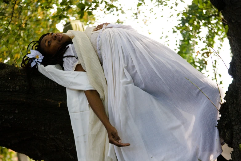 an african woman in white robes, leaning on a large tree