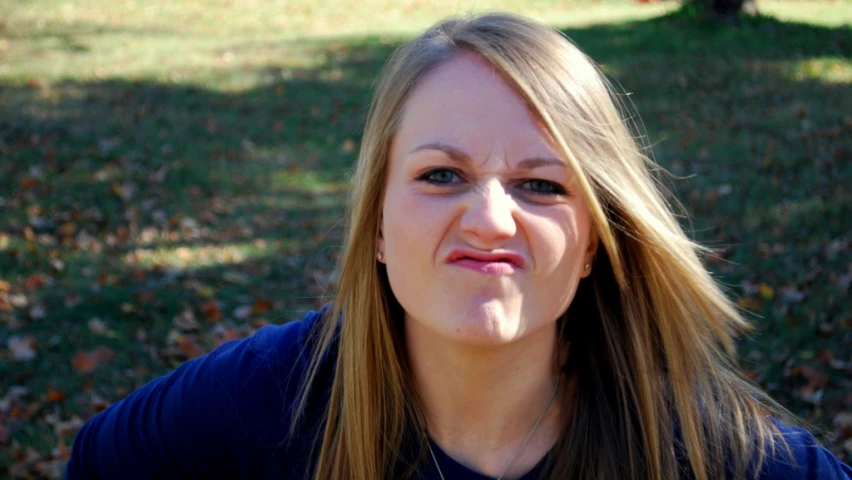 a woman is making a goofy face while standing in front of a park