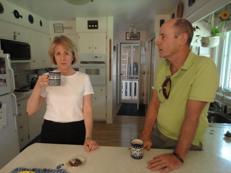 a man and a woman stand at the kitchen counter, drinking from cups