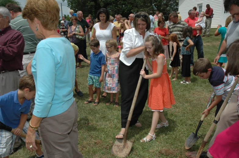 woman holding long shovel in grassy area with crowd of people