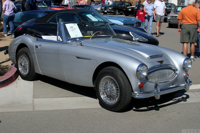 an old, silver, classic sports car sits parked outside