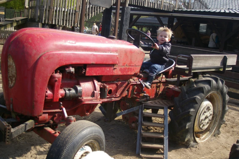 the small boy is sitting on the large tractor