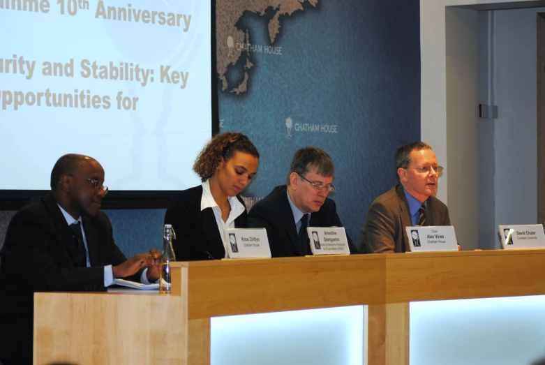 four people sit at a conference table, two are speaking