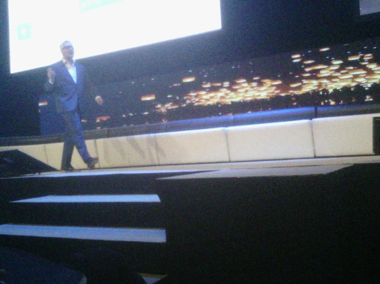 a man standing on stage in front of a projection screen