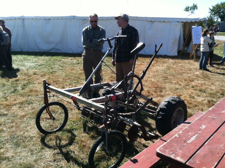 two men in the field talking about an old fashioned bike