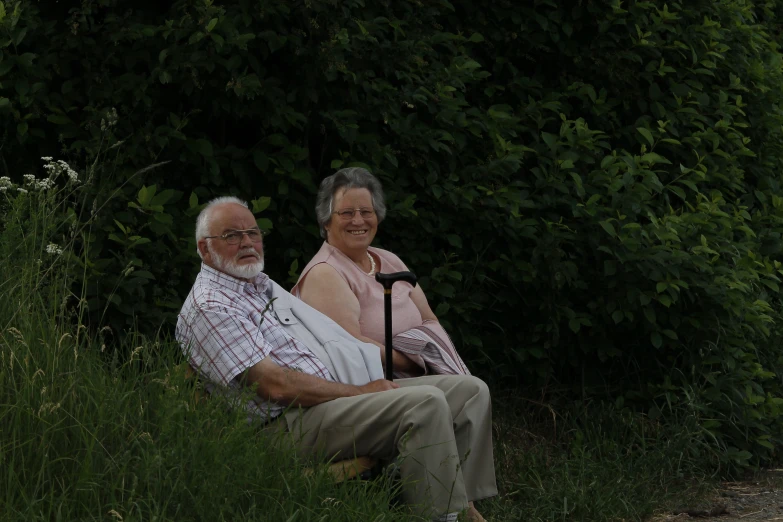 an old couple relaxing on a bench near a bush