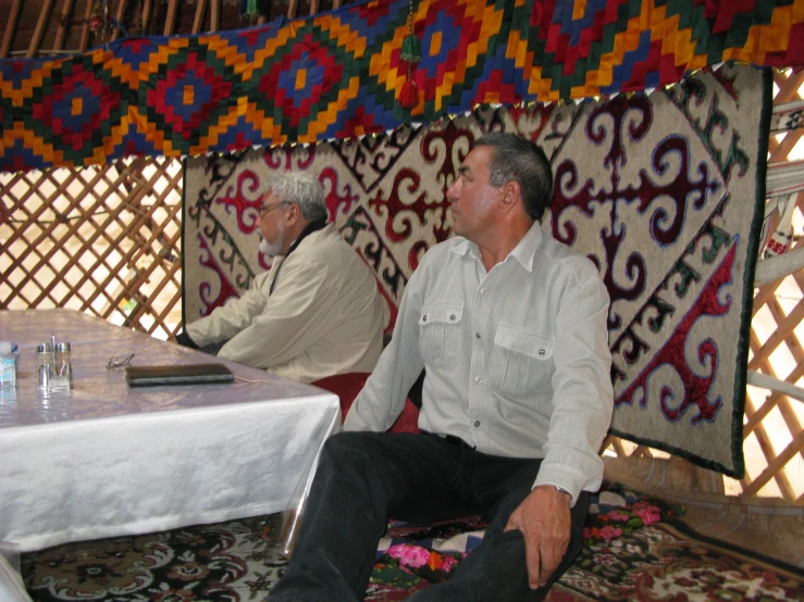 two men sitting at a table while the man talks on a cell phone