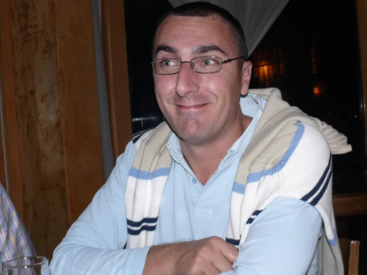 a man in glasses sitting at a table with a glass