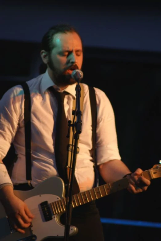 a man in vests and tie playing guitar